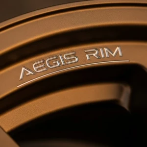 AEGIS RIM forged wheel lip in bronze finish—where precision engraving meets advanced coating for durability and design expression. Bronze-finished lip engraving on AEGIS RIM forged alloy wheel—illustrating precision marking and multi-layer surface coating.