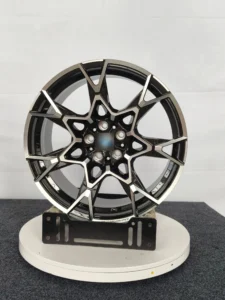 Stylish black and silver alloy wheel displayed on a rotating stand, showcasing its intricate design and craftsmanship.