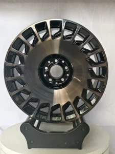 Stylish black alloy wheel displayed on a stand, showcasing intricate designs and a polished finish. Ideal for car enthusiasts.