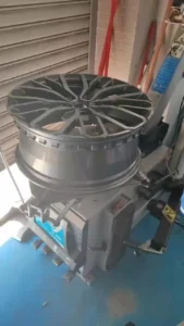 Rim and tire mounting machine in a workshop, showcasing a black alloy wheel being prepared for installation.