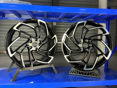 Two sleek black alloy wheels displayed on a blue shelf, showcasing modern design and polish.
