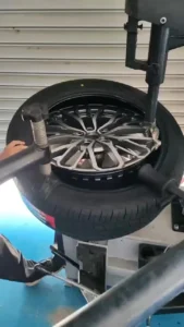 Mechanic mounting a tire onto a sleek alloy wheel using specialized equipment in an auto shop.