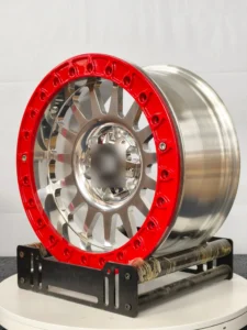Glossy metallic wheel with a red rim and intricate design, displayed on a rotating stand against a neutral background.