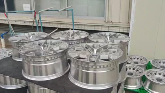 Set of polished aluminum car rims displayed outdoors, showcasing sleek design and craftsmanship on a black surface.
