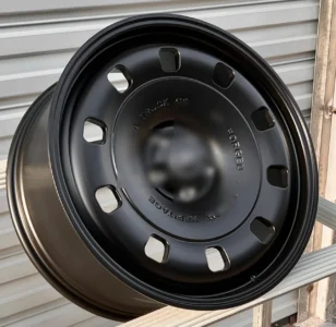 Close-up of a black forged truck wheel showcasing its unique design and sturdy construction against a metal backdrop.