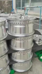 Stack of polished aluminum car rims displayed in an industrial setting, showcasing their sleek design and craftsmanship.